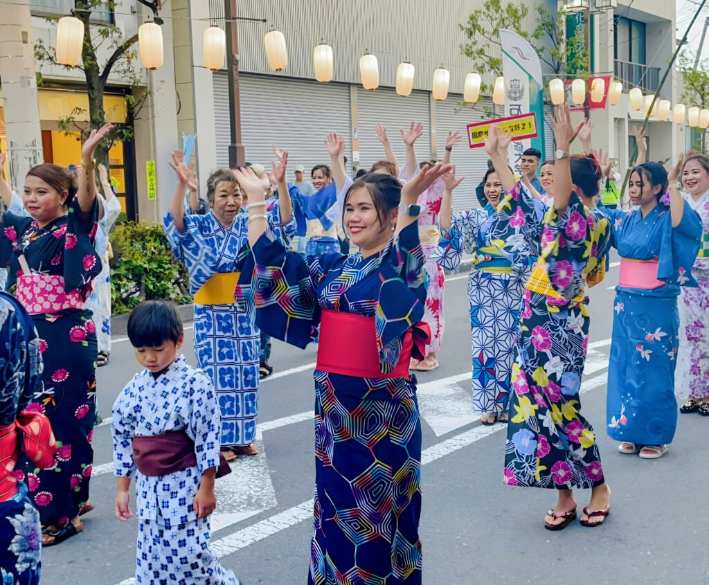People in colorful yukata dancing joyfully at a Japanese summer festival under lantern decorations.