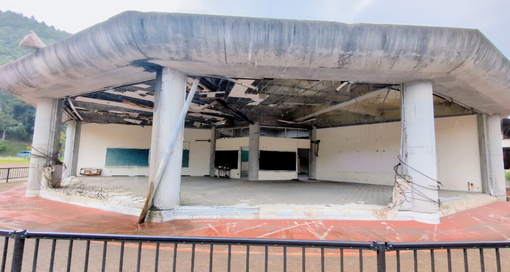Okawa School Tsunami Memorial – Stories of Hope and Resilience Collapsed classroom with broken roof beams inside Okawa Elementary School ruins after the 2011 tsunami.