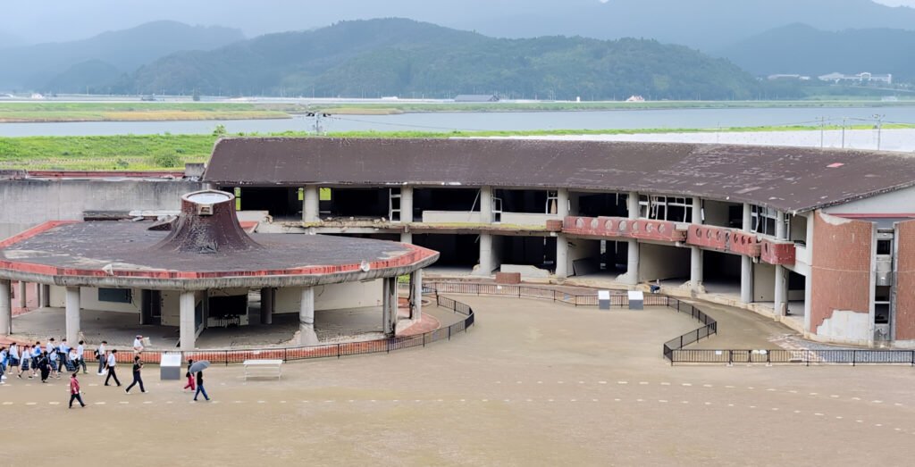 Okawa School Tsunami Memorial – Stories of Hope and Resilience Okawa Elementary School courtyard with the Kitakami River visible in the background.