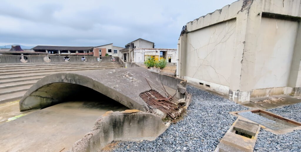 Okawa School Tsunami Memorial – Stories of Hope and Resilience Curved collapsed structure in front of Okawa Elementary School ruins in Ishinomaki, a reminder of the 2011 disaster.