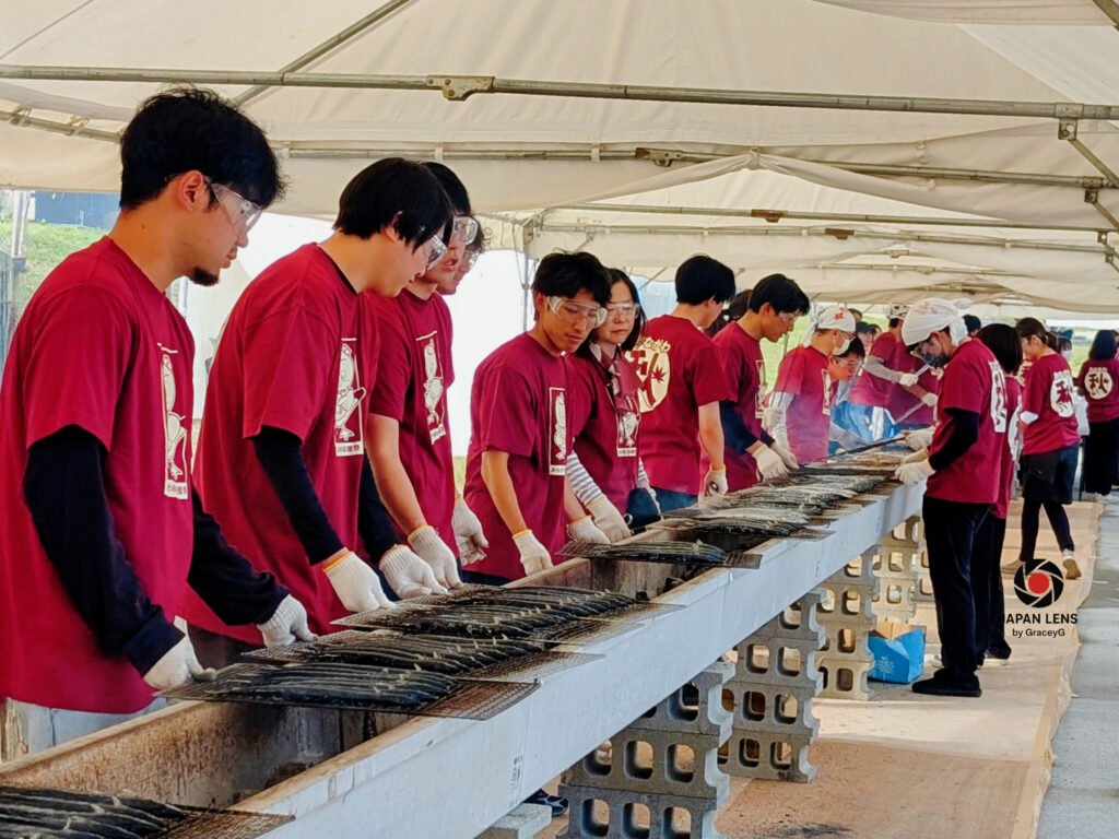 Onagawa Harvest Festival — The Autumn Where Smoke Meets the Sea Volunteers in matching red shirts grilling rows of Pacific saury at Onagawa Harvest Festival 2025, Miyagi, Japan — teamwork, tradition, and the aroma of autumn captured by Japan Lens by GraceyG.