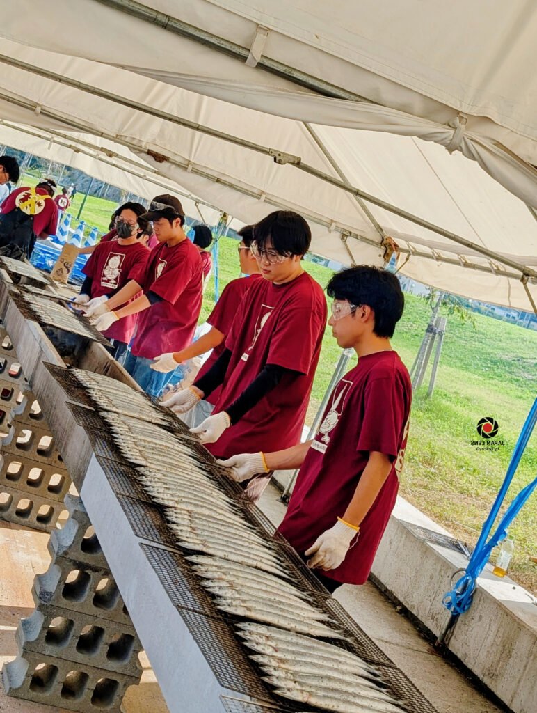 Volunteers grilling fresh Pacific saury during Onagawa Harvest Festival 2025 in Miyagi, Japan — rows of fish cooking over charcoal, symbolizing the town’s autumn gratitude and unity. Captured by Japan Lens by GraceyG.