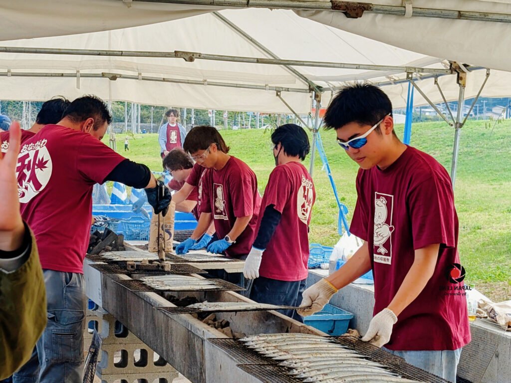 Focused volunteers grilling rows of Pacific saury during Onagawa Harvest Festival 2025, Miyagi, Japan — a moment of teamwork, tradition, and gratitude captured by Japan Lens by GraceyG.