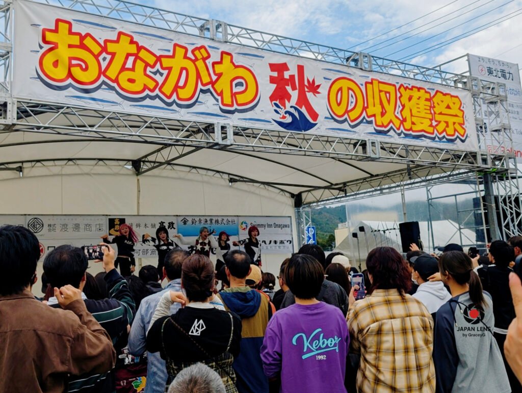 Stage view of Onagawa Harvest Festival 2025 with the banner “おながわ 秋の収穫祭” (Onagawa Autumn Harvest Festival) and a crowd gathered to celebrate Japan’s autumn season in Miyagi Prefecture. Captured by Japan Lens by GraceyG.