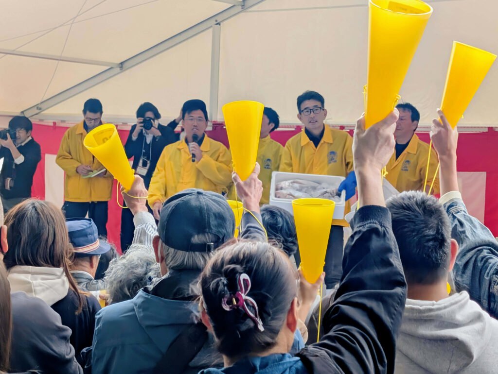 Auction leaders and crowd raising yellow cones during the Ishinomaki Taigyō Matsuri seafood auction